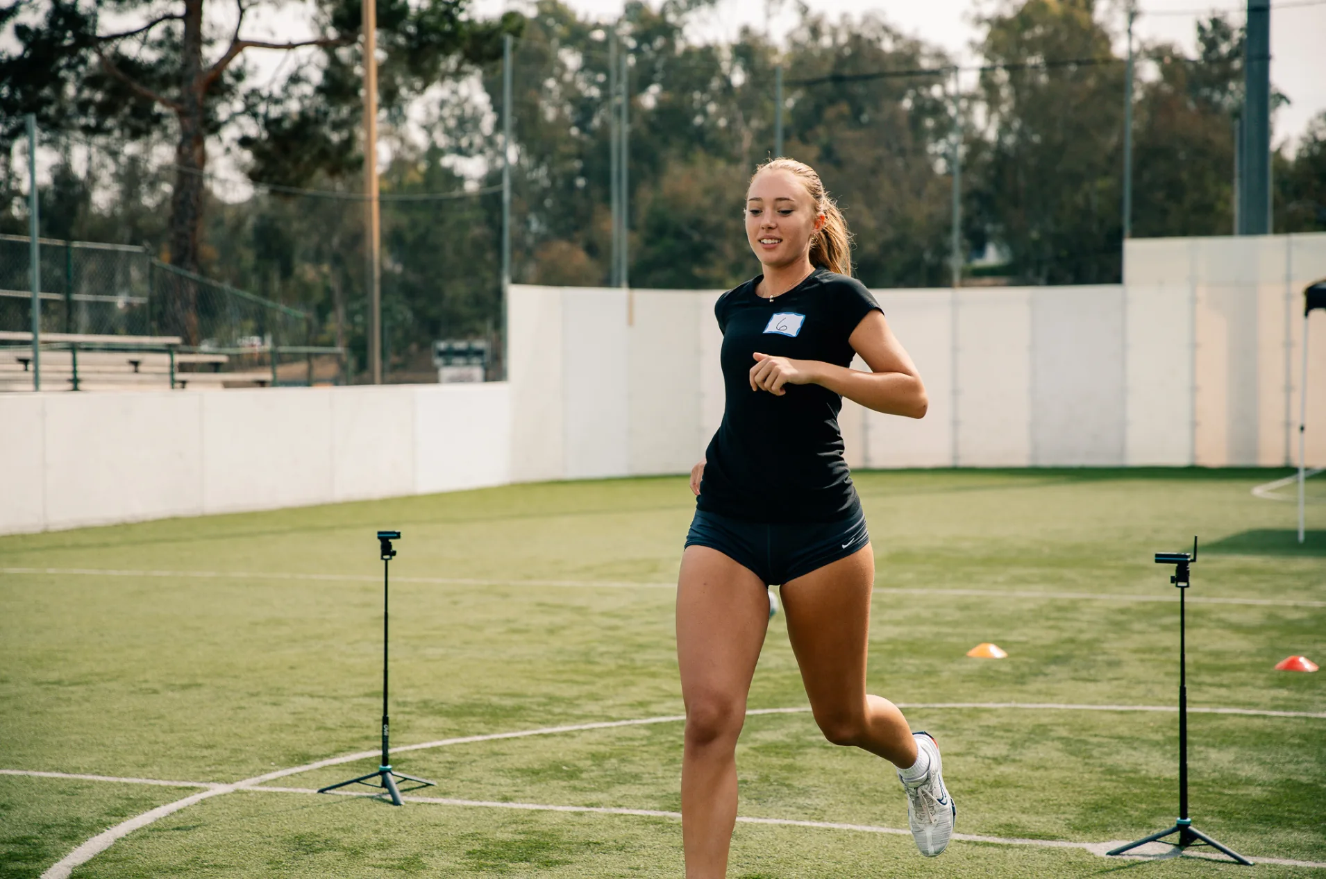 A young female athlete sprinting between electronic timing gates on a turf field